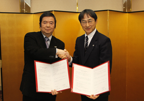 協定書を手に握手を交わす北野学長と長野社長