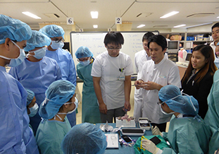 糸結び，縫合体験で外科医の説明を熱心に聞く参加者